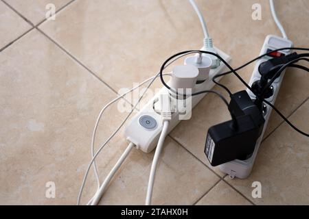 Überlastete Stromversorgungsplatinen. Steckdosenleisten mit verschiedenen Steckern auf weißem Boden. Konzept der Gefahr Gefahr Überlaststrom elektrisch Stockfoto