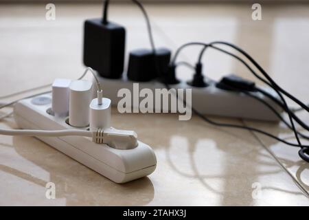 Überlastete Stromversorgungsplatinen. Steckdosenleisten mit verschiedenen Steckern auf weißem Boden. Konzept der Gefahr Gefahr Überlaststrom elektrisch Stockfoto