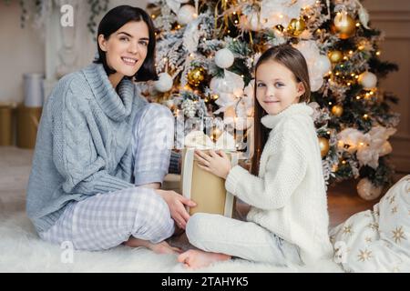 Mutter und Tochter mit Weihnachtsgeschenk an einem Weihnachtsbaum in gemütlicher Kleidung Stockfoto