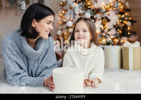 Mutter und Tochter lächeln mit einem Weihnachtsgeschenk, Baum mit Lichtern geschmückt Stockfoto