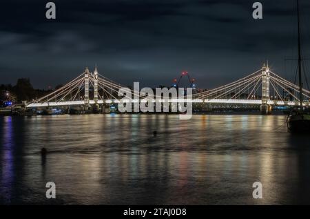 London, Großbritannien - 20. November 2023 - nächtlicher Blick auf die Albert Bridge mit Flutlicht von der Chelsea Bridge mit der Reflexion des Lichts im sehr ruhigen Wasser des Flusses Stockfoto