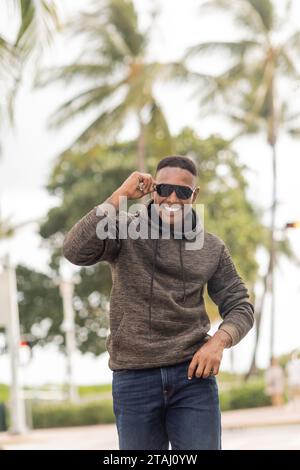 Fröhlicher afroamerikaner in Hoodie und Jeans mit Sonnenbrille auf der Straße in Miami Stockfoto