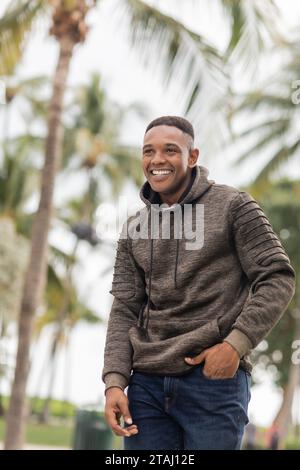 Glücklicher afroamerikanischer Mann im Hoodie, der mit der Hand in der Jeans-Tasche steht Stockfoto