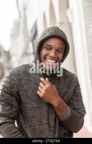 Fröhlicher afroamerikanischer Mann in Kapuzenpullover, der wegschaut, während er draußen lächelt Stockfoto