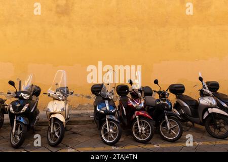 Mehrere Motorroller parkten vor einer hellgelben Wand auf einem Bürgersteig in Florenz, Italien. Stockfoto