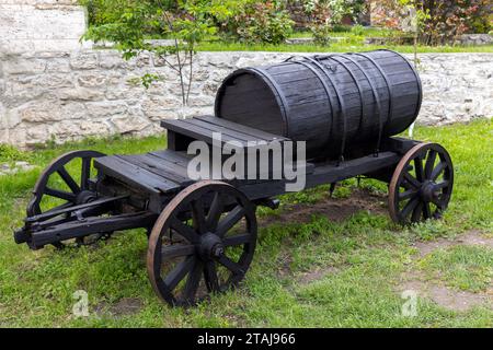 Ein alter Holzwagen mit Fass steht auf grünem Gras in der Nähe einer ländlichen Steinmauer Stockfoto