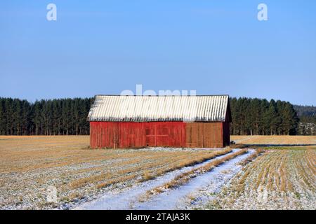 Rote Holzscheune auf dem Feld an einem sonnigen Novembertag mit frisch gefallenem Schnee auf dem Boden. Stockfoto