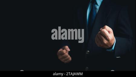 Geschäftsmann im Anzug steht und macht eine Faustgeste auf dunklem Hintergrund. Stockfoto