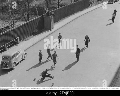 Fußball auf der Straße. Eine Gruppe Jungs spielt Fußball auf der Straße an einem Sommertag. Sie haben zwei Pflastersteine gelegt, um zu markieren, wo das Fußballtor ist. Ein harmloses Vergnügen für die Jugendlichen. Wenn ein Auto kam, stoppte das Spiel, und als das Auto vorbei war, ging es weiter. Stockfoto