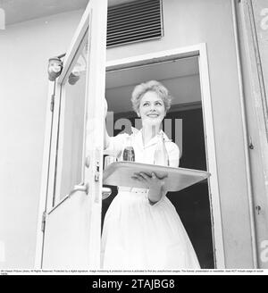 Eine junge Frau arbeitet als Kellnerin in einer Konditorei und kommt mit einem Tablett mit alkoholfreien Getränken zur Tür. 1958 Stockfoto