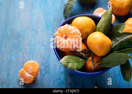 Frische saftige Mandarinen in einer blauen Keramikschale auf hölzernem Hintergrund. Stockfoto