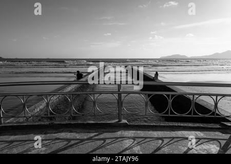 Stadt Santos, Brasilien. Water Channel Bridge Nr. 6. Die Leute genießen den Strand an der Wand. Bucht und Horizont im Hintergrund. Schwarzweißbild Stockfoto