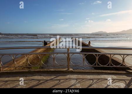 Stadt Santos, Brasilien. Wasserkanalbrücke Nr. 6. Die Leute genießen den Strand an der Wand. Santos Bucht und Horizont im Hintergrund. Blauer Himmel mit Wolken. Stockfoto