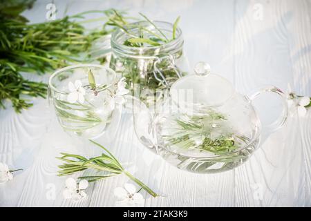 Galium-Aparine-Klinge, Katzengras, Stachelgras, rotkehlchen, Sticky Willy. Tasse grüner Tee mit Blumen auf Holztisch, Nahaufnahme. Stockfoto