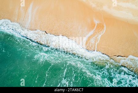 Blick aus der Vogelperspektive auf den Sandstrand und das türkisfarbene Meer. Blick von oben auf die Meereswellen, die an sonnigen Tagen ans Ufer gelangen. Stockfoto