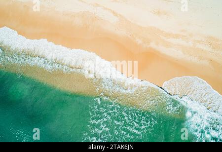 Blick aus der Vogelperspektive auf den Sandstrand und das türkisfarbene Meer. Blick von oben auf die Meereswellen, die an sonnigen Tagen ans Ufer gelangen. Stockfoto