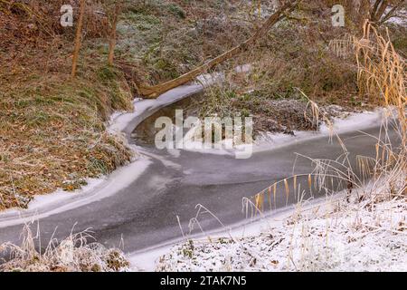 Einmündung eines Ribulets in einen kleinen Bach, der im Winter mit Eis gefroren ist Stockfoto