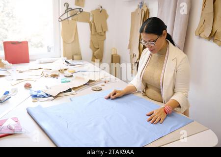 Der Designer arbeitet mit blauem Stoff auf dem Schneidtisch Stockfoto