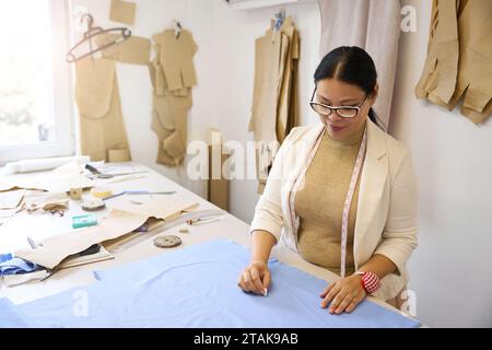 Die Designerin arbeitet mit blauem Stoff auf dem Schneidetisch Stockfoto