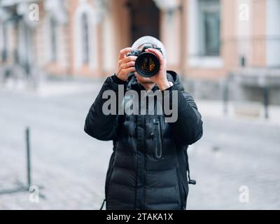 Männlicher Fotograf macht ein Foto mit einer professionellen Digitalkamera vor dem Hintergrund der Stadtstraße. Stockfoto