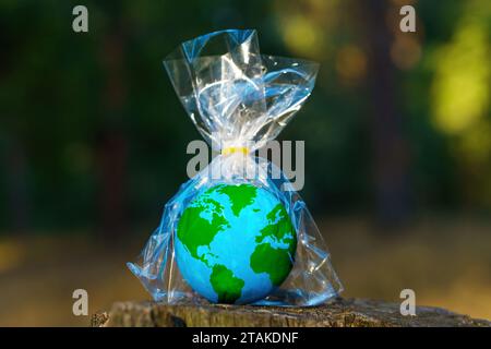 Kleines Kugelmodell in transparenter Kunststoffverpackung sitzt auf einem Waldstumpf. Plastische Verschmutzung und umweltbewusstseinsbedingte Verwölbung Stockfoto