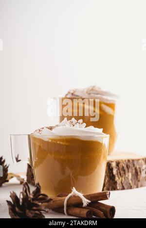 Kürbis-Gewürz-Latte in einem Glasbecher mit Schlagsahne und Zimt, wärmerem Herbst und Winter gemütliches Heißgetränk Stockfoto