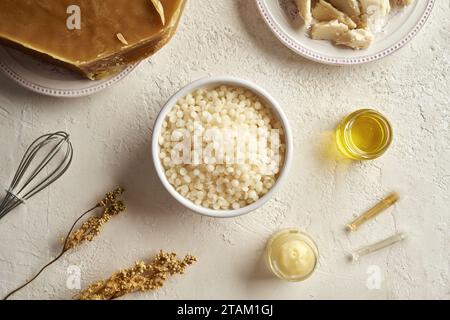 Bienenwachs-Pellets in einer Schüssel mit ätherischen Ölen, Kräutern und Sheabutter, Draufsicht Stockfoto