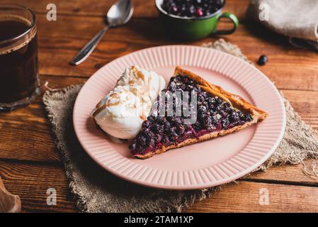 Eine Scheibe frisch gebackene Amelanchier Beeren Galette und zwei Schaufeln Vanille-Eis auf dem Teller über dem rustikalen Tisch Stockfoto