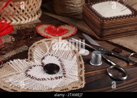 Herzförmige Stücke aus Sackleinen-Stoff mit verschiedenen Stichen und Nähwerkzeugen auf Holztisch, Nahaufnahme Stockfoto