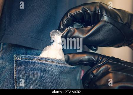 Der Polizist steckt die Drogen in die Tasche des jungen Mannes. Suche nach einem Drogenabhängigen. Nahaufnahme einer Tüte Kokain in seinen Händen. Arzneimittelpest. Eine Hand zieht einen Stockfoto