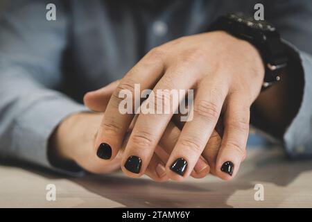 Ein Mann mit bemalten Nägeln. Die Gestaltung der männlichen Nägel. Männer Maniküre. Die Nägel sind in modischer schwarzer Farbe lackiert Stockfoto