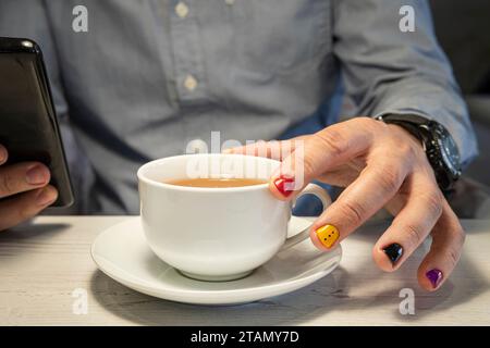 Ein junger Hipster mit bemalten Nägeln trinkt Tee in einem Café. Teepausen-Konzept Stockfoto