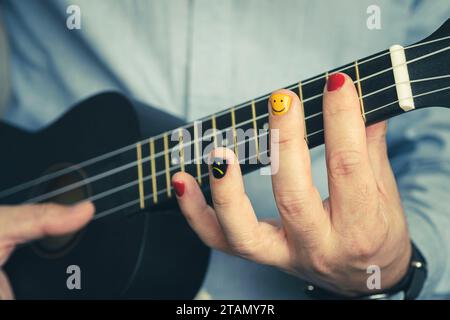 Ein Musiker mit bemalten Fingernägeln spielt eine Ukulele in Nahaufnahme. Ein musikalisches Konzept. Ein Mann mit bemalten Nägeln. Die Gestaltung der männlichen Nägel. Männer Maniküre. Stockfoto