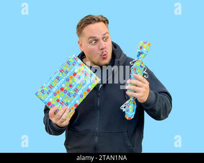 Ein erstaunt aussehender Mann, der zwei blaue Schachteln mit Geschenken in sich hält, im Stil von Candycore Stockfoto
