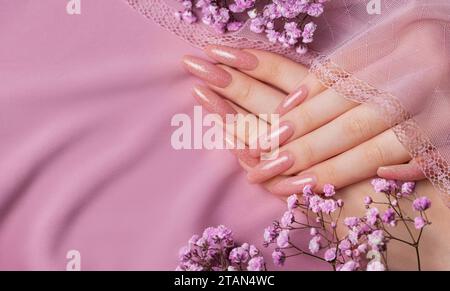 Weibliche Hände mit schöner Maniküre mit Gipsofila-Blüten auf rosa Seide Stockfoto