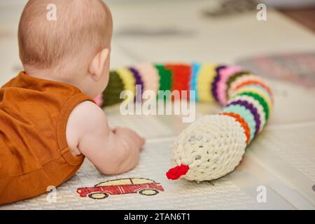 Das Baby spielt mit einem gestrickten Spielzeug im Kinderzimmer Stockfoto