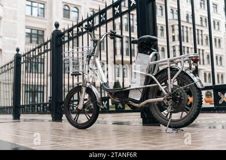 Ein modernes Elektrofahrrad parkt auf einer belebten Straße. Das Motorrad ist mit einem Laderaum ausgestattet, wodurch es für eine effiziente Lieferung geeignet ist Stockfoto