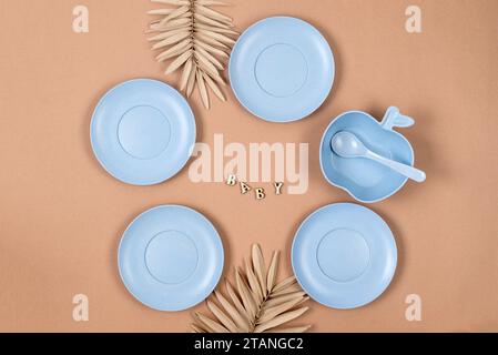 Babytisch-Einstellung. Silikon-Set mit blauem Teller, Tasse, Besteck auf pastellbeigem Hintergrund. Platz für Text, Kopierraum. Stockfoto