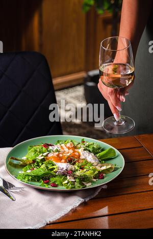 Salat mit Stracciatella und Persimmon und einem Glas Weißwein. Essen auf dem Teller. Restaurant-Menü-Konzept. Kopierbereich. Flache Lagen. Stockfoto