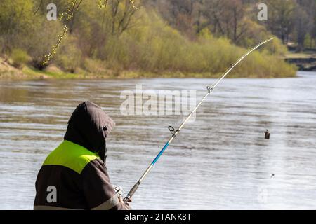 Ein Angler fängt Fische mit mehreren Angelruten am Ufer des Flusses Stockfoto