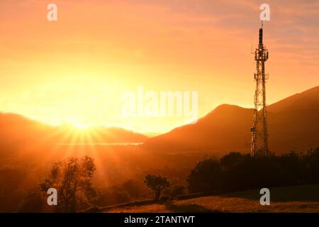Telekommunikationsmast auf goldenem Sonnenuntergang Hintergrund in den Bergen. Wunderbarer Sonnenuntergang im Lake District (Keswick) Stockfoto