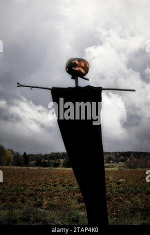 Gruselige Halloween-Vogelscheuche mit schwarzem Tuch und geschnitztem Kürbis als Kopf, im Feld mit dramatischem Himmel als Hintergrund. Stockfoto