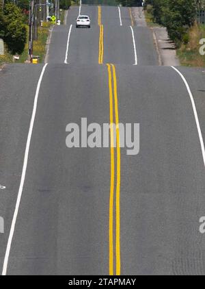 Die Straße vor Ihnen ist eine Reihe von gewellten Hügeln mit doppelten gelben Mittellinien, die in der Ferne verschwinden. Stockfoto