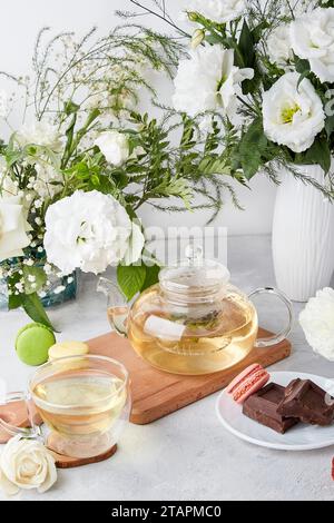 Ästhetischer Tisch - Teekanne, Tasse, Desserts, weiße Blumen - Zeit für sich, gemütliches Hauskonzept Stockfoto