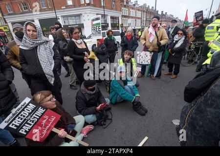 London, Großbritannien. Dezember 2023. Am Ende eines waffenstillstandsmarsches in Gaza zu einer Kundgebung in Brixton umzingelte eine Menschenmenge einen Polizeiwagen mit einem jungen Teenager, der wegen eines angeblich antisemitischen Plakats verhaftet wurde und rief: „Lass sie gehen!“ Und den Van daran hindern zu gehen. Die Polizei stritt sich etwa 45 Minuten lang mit den Demonstranten und brachte schließlich fast hundert Polizisten ein, die die Menge zurück auf den Bürgersteig drängten, damit der Van abfahren konnte. Peter Marshall/Alamy Live News Stockfoto