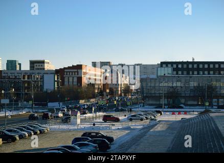 Nahaufnahme des Stadtzentrums mit vielen Gebäuden. Parkplatz mit vielen Autos neben der befahrenen Autobahn und dem blauen Himmel Stockfoto