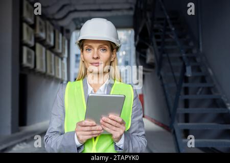 Porträt einer jungen Ingenieurin, Bauarbeiterin, Architektin mit Schutzhelm, reflektierender Weste und Tablet. Er schaut ernsthaft in die Kamera. Stockfoto