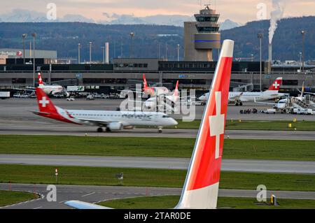 Vertikales Heck eines Airbus der Swiss International Air Lines mit dem Schweizer Kreuz, hinter einem Flugzeug der Airline Helvetic taxiyng zum Start, Zuri Stockfoto