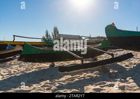 Einfache Fischerboote an einem Sandstrand in der Nähe des kleinen Dorfes Madagaskar, die Sonne scheint im Hintergrund Stockfoto