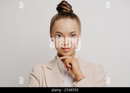 Selbstbewusste Geschäftsfrau in einem beigefarbenen Blazer mit einer durchdachten Handbewegung, die Professionalität widerspiegelt Stockfoto